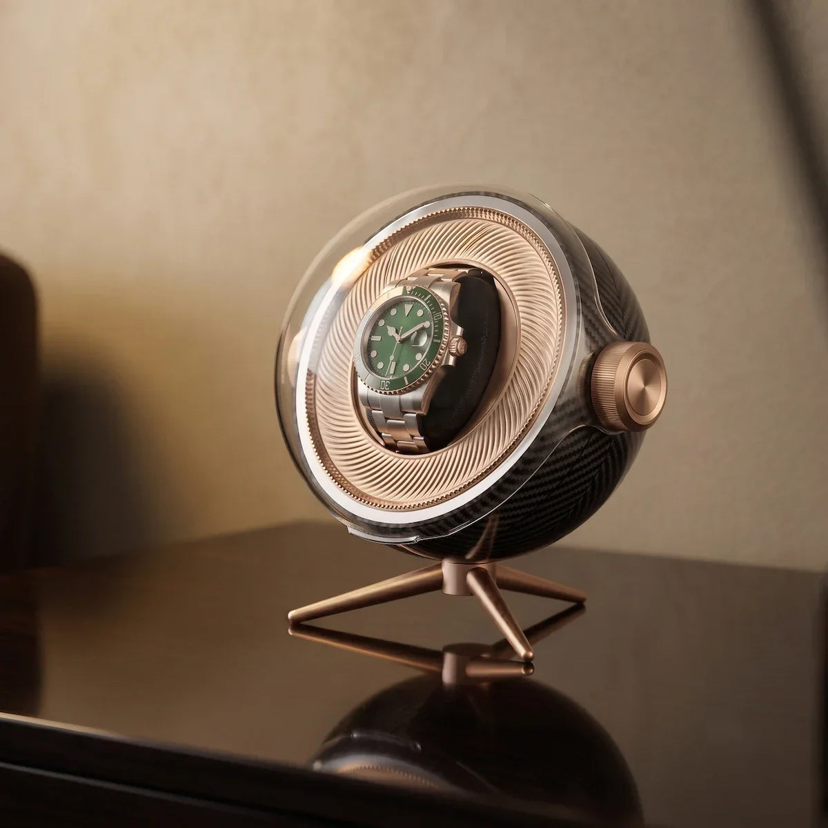 Tripode Solo automatic watch winder in carbon fibre with a green-dial watch on a gold tripod stand.