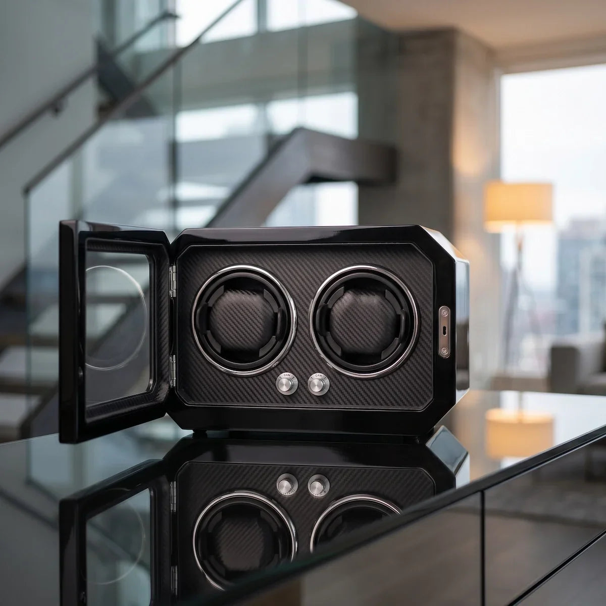 Watch winder for 2 watches in black carbon fibre with a glass door and LED lighting, placed on a modern table.