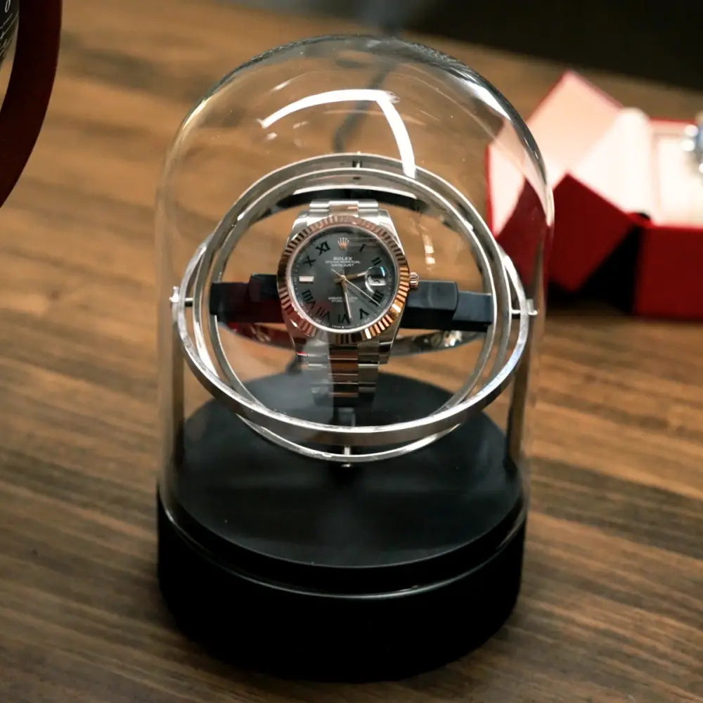 Astronome automatic winder in silver steel under a glass dome, modern rotating design for a luxury watch.