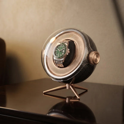 Tripode Solo automatic watch winder in carbon fibre with a green-dial watch on a gold tripod stand.