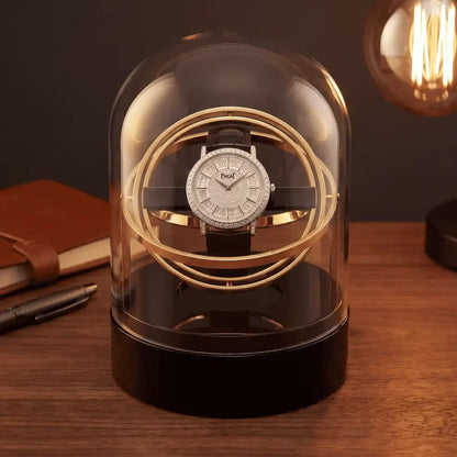 Gold automatic winder for one watch, under a glass dome with elegant black base on a wooden desk.