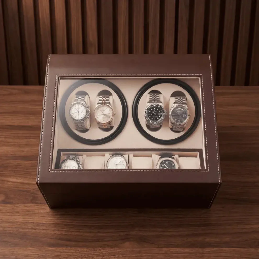 Brown leather watch winder with 4 automatic rotors, 6 storage slots and glass lid on a wooden background.