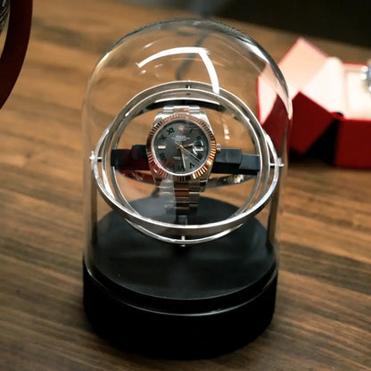 Astronome automatic winder in silver steel under a glass dome, modern rotating design for a luxury watch.