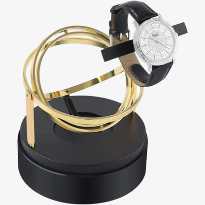 Astronome gold automatic watch winder with modern spherical design on a black base, with a leather-strap watch.